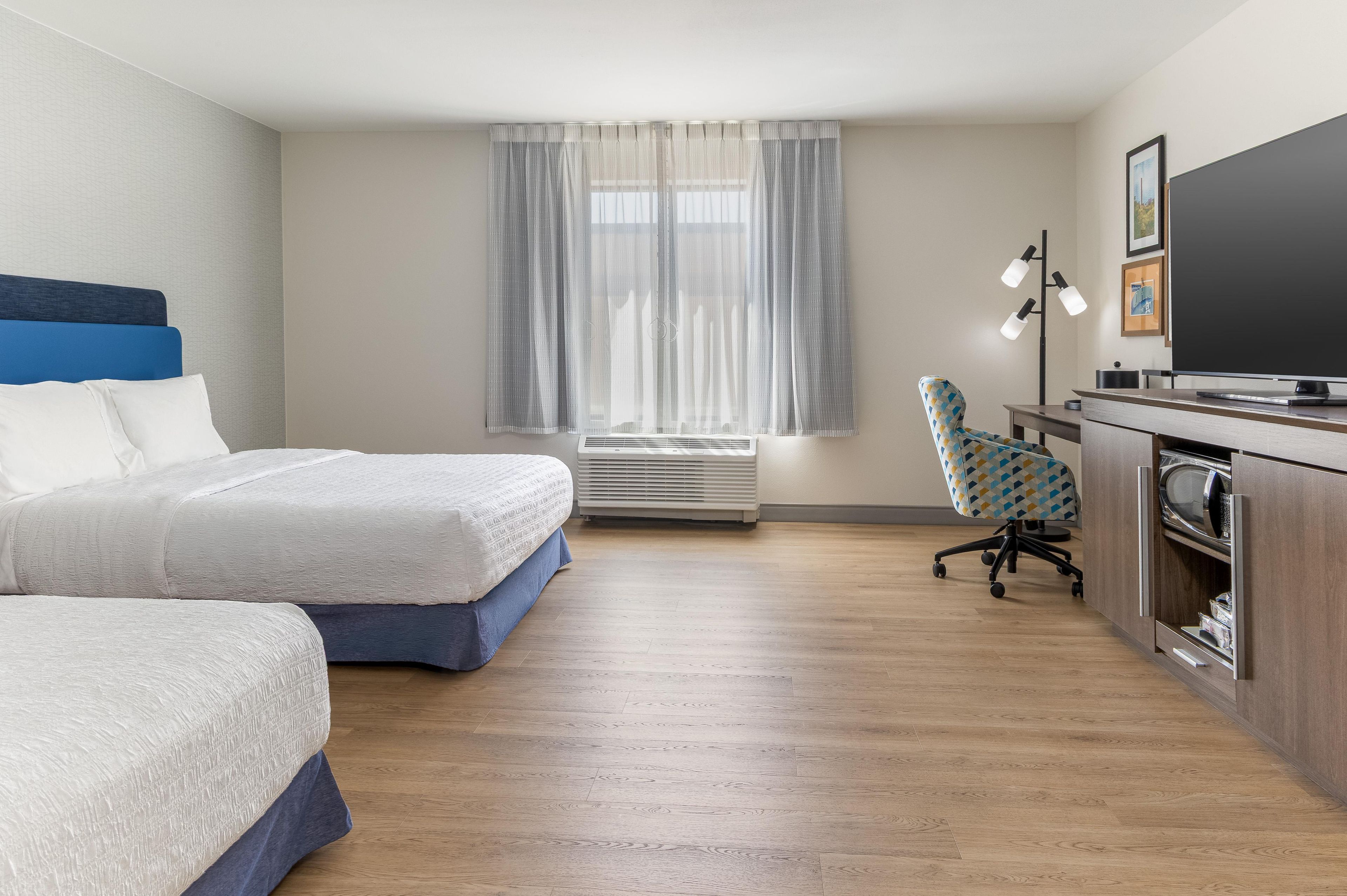 A hotel room with two beds, a desk with a computer, a chair, a television, and a window with curtains.