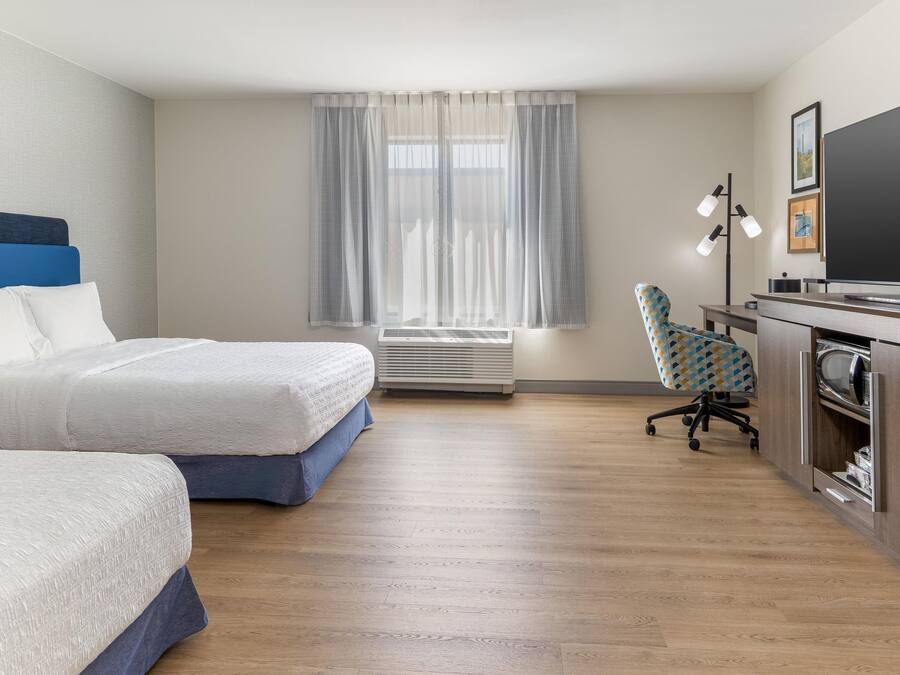 A hotel room with two beds, a desk with a computer, a chair, a television, and a window with curtains.