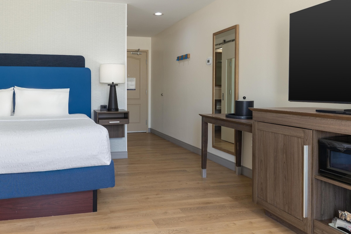 A hotel room with a bed, bedside table, lamp, and a television.