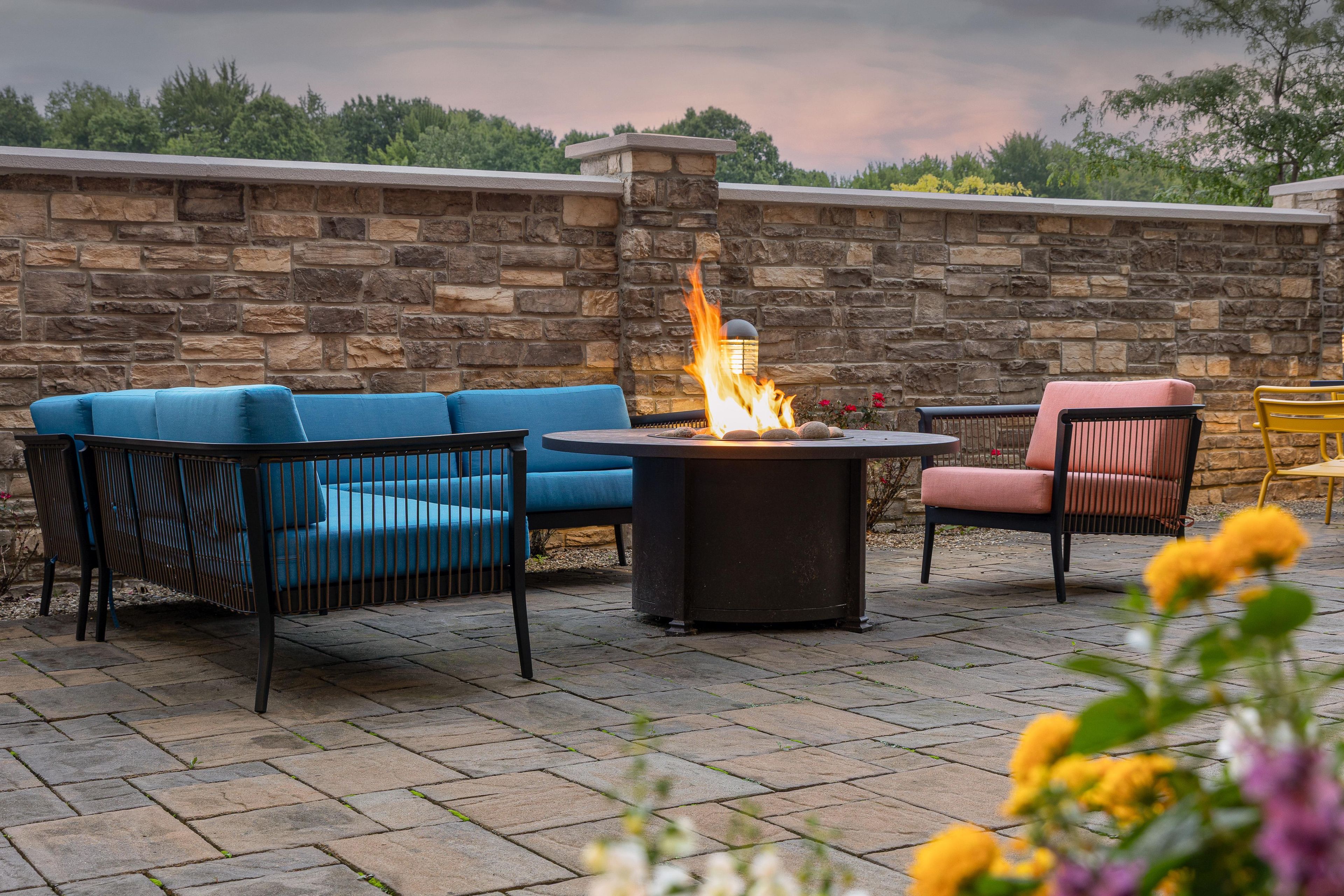 A patio with stone flooring, a fire pit, and outdoor furniture including a blue sofa and a pink chair.