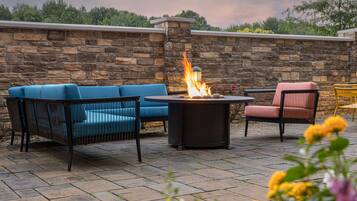 A patio with stone flooring, a fire pit, and outdoor furniture including a blue sofa and a pink chair.