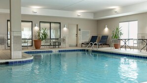 An indoor swimming pool with clear water, surrounded by lounge chairs and potted plants.