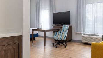 A room with a wooden desk, a chair, a television, and an air conditioning unit.