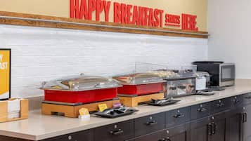 A breakfast buffet setup with labeled containers for French Toast Sticks and Maple-Snicked, a microwave, and a coffee machine.