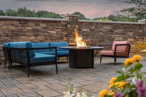 Un patio con suelo de piedra, un brasero y mobiliario exterior, incluyendo un sofá azul y una silla rosa.