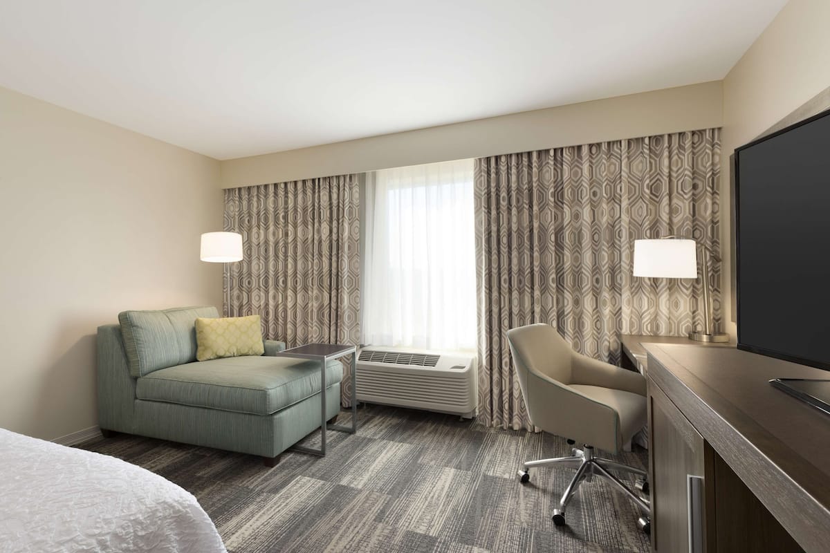 Quarto de hotel com sofá, poltrona, escrivaninha e televisão de tela plana.
