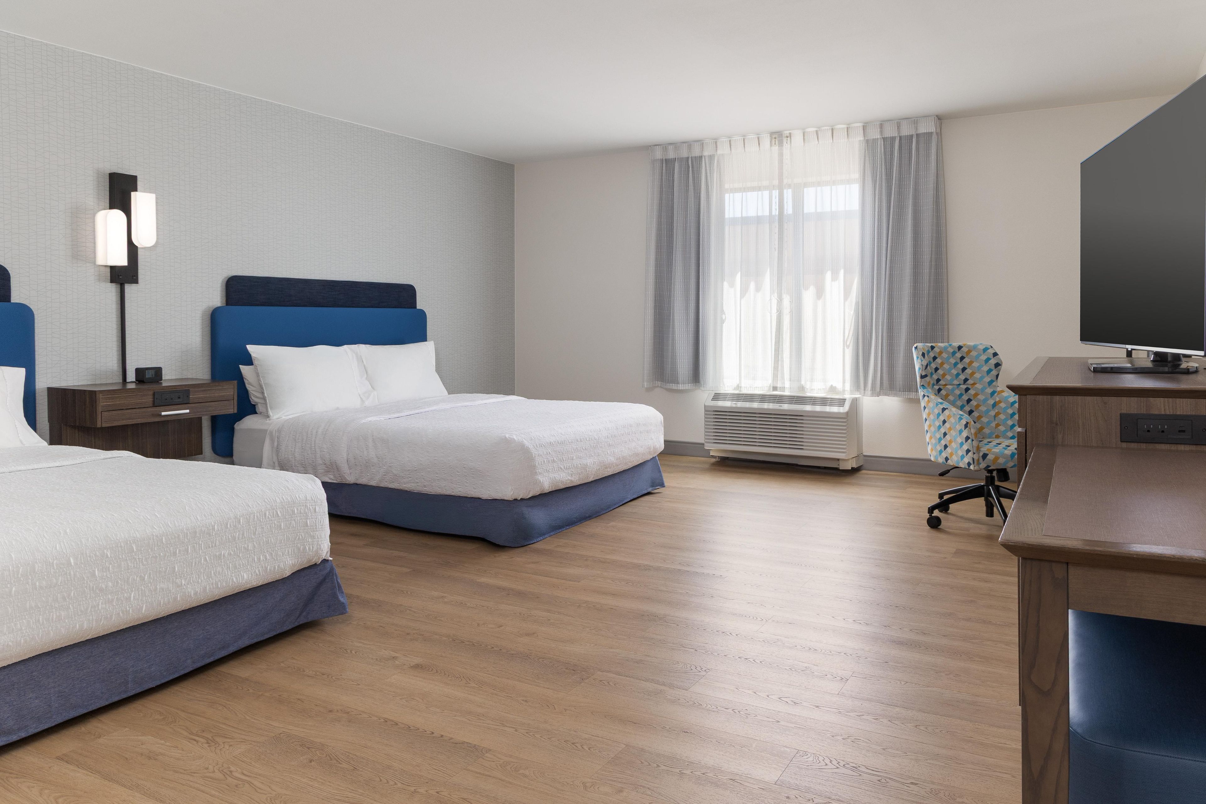A hotel room with two beds, a desk with a television, and a window with curtains.