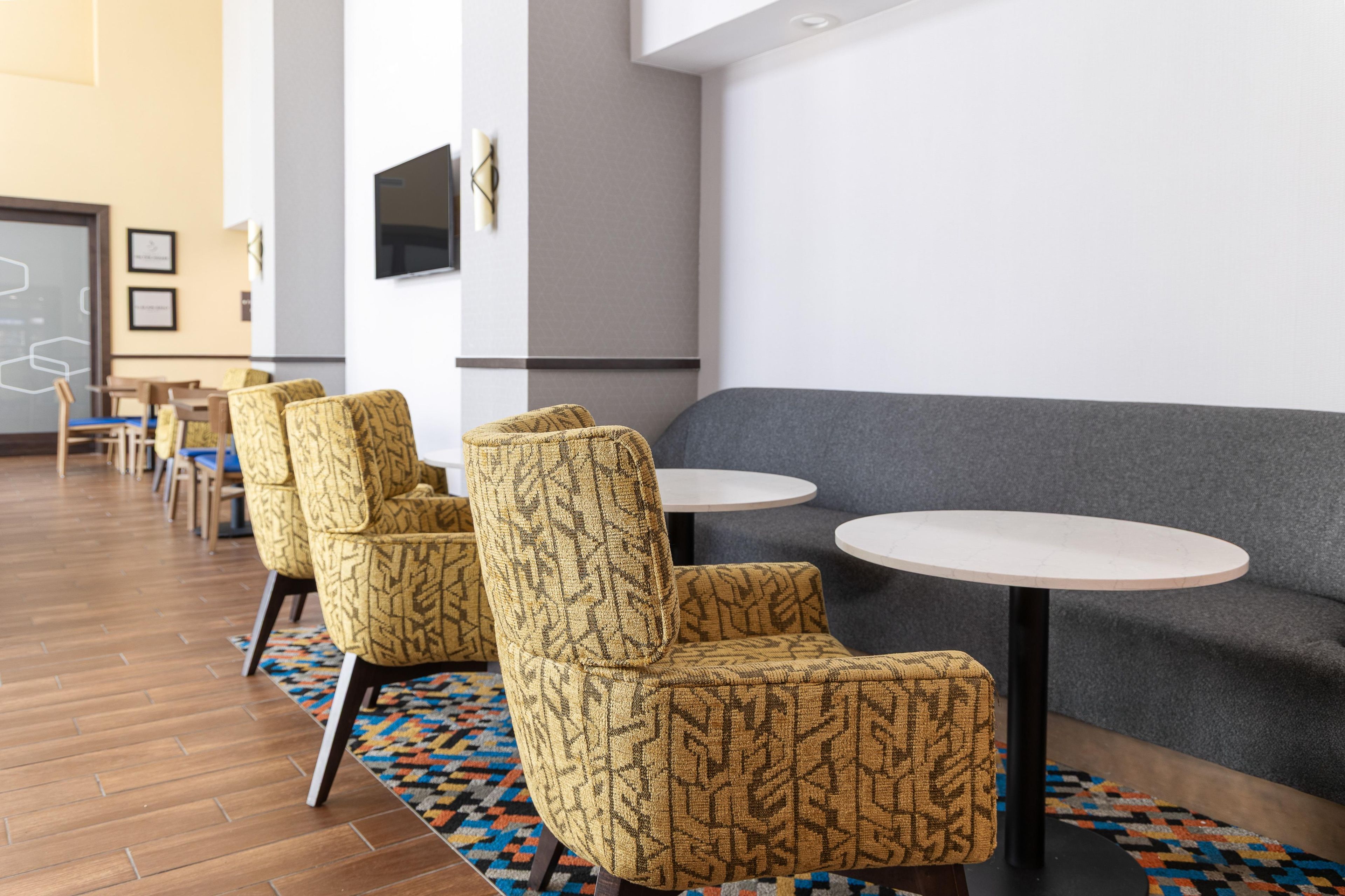 Un área de estar moderna con sillones estampados, un sofá gris y pequeñas mesas redondas.