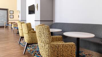 Un área de estar moderna con sillones estampados, un sofá gris y pequeñas mesas redondas.