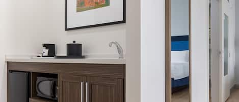 A modern bathroom with a sink, a coffee machine, and a framed picture on the wall.