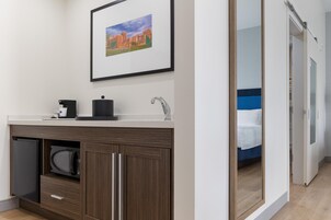 Un baño moderno con un lavamanos, una cafetera y un cuadro enmarcado en la pared.