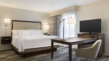 A hotel room with a bed, bedside tables, a desk, a chair, a television, and a lamp.