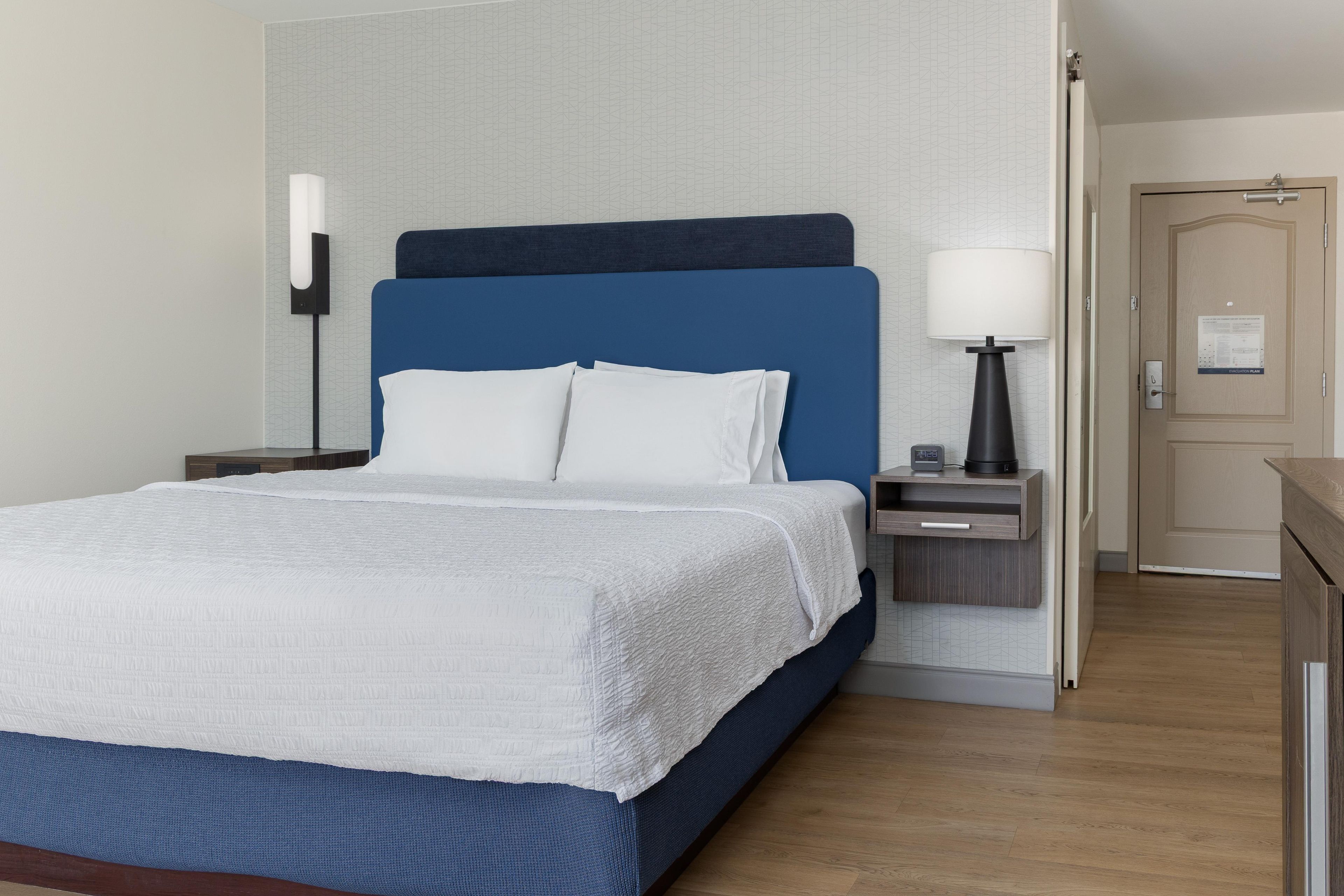 Una habitación de hotel con cama, mesita de noche, lámpara y puerta.
