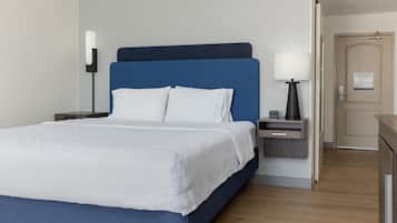 Una habitación de hotel con cama, mesita de noche, lámpara y puerta.
