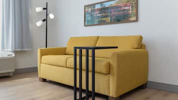 Un sofá amarillo con estructura negra, una lámpara de pie y un cuadro en la pared.