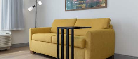 A yellow sofa with a black frame, a floor lamp, and a painting on the wall.