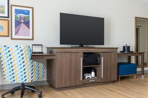 Une chambre d’hôtel équipée d’un bureau en bois, d’un téléviseur à écran plat, d’un fauteuil à motifs, d’une machine à café et d’un four à micro-ondes.