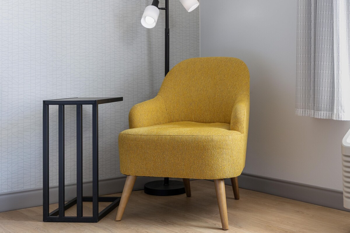 Ein gelber Sessel mit Holzbeinen, ein schwarzer Metall-Beistelltisch und eine Stehlampe mit weißen Lampenschirmen.
