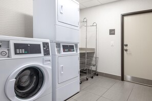 A laundry room with stacked washing machines and dryers, a metal cart, and a linen storage sign on the wall.