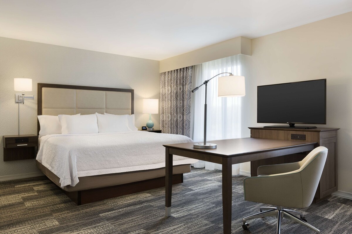 A hotel room with a bed, desk, chair, TV, lamp, and nightstand.