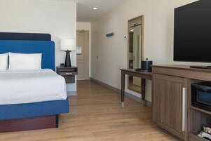 A hotel room with a bed, bedside table, lamp, and a television.
