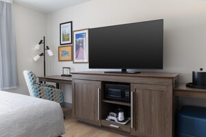 Habitación de hotel con cama, escritorio, televisor de pantalla plana, microondas y cafetera.