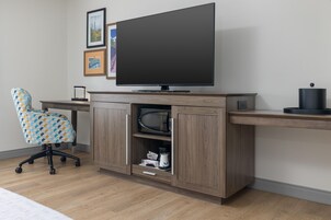 Un espacio de oficina moderno con una televisión de pantalla plana, una silla de oficina estampada y un escritorio de madera con estante.