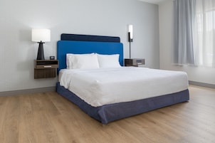 A hotel room with a bed, nightstands, a lamp, and a window with curtains.