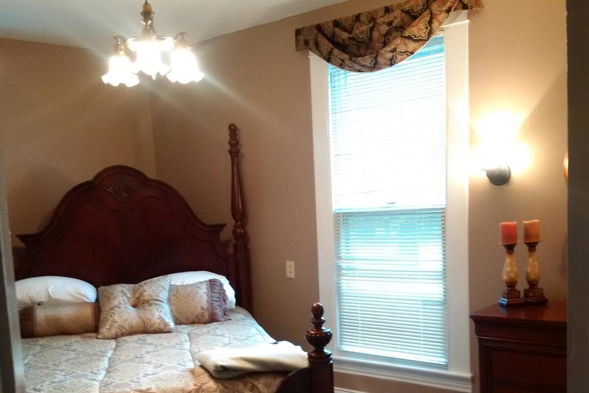 Un dormitorio con una cama grande, cabecera de madera, ventana con persianas, mesita de noche con velas y un candelabro.