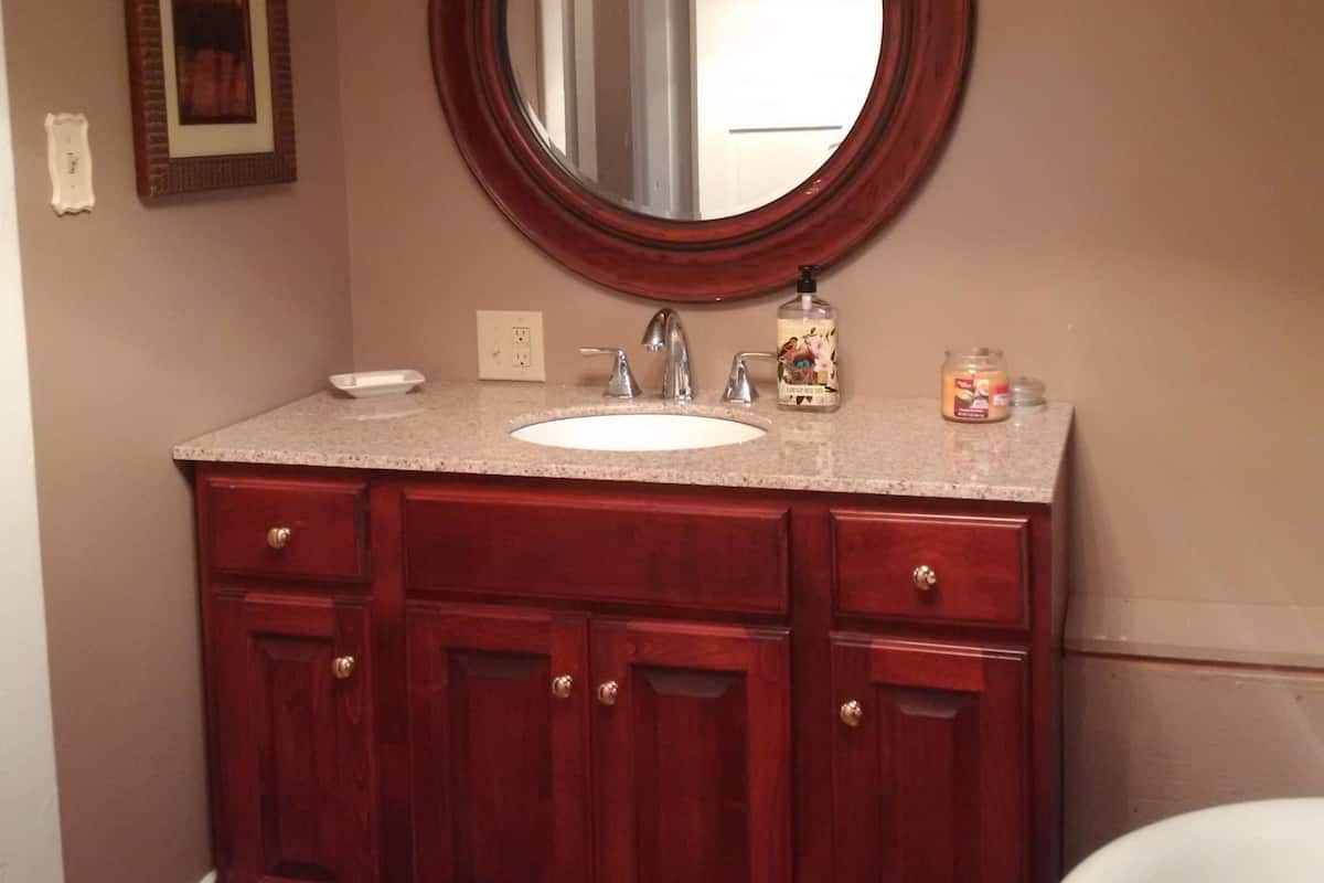 Un baño con un espejo redondo, un lavabo blanco y armarios de madera.