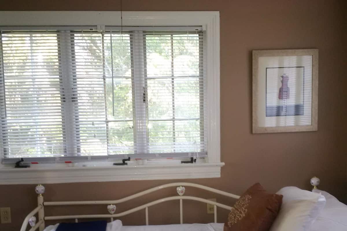 Un dormitorio con cama, ventana con persianas y un cuadro en la pared.