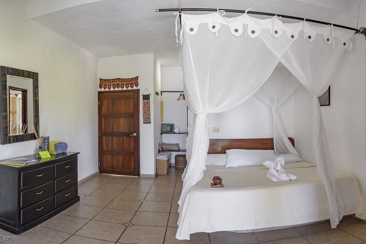 A bedroom with a four-poster bed, a nightstand, a dresser, and a mirror.