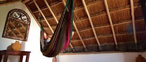 A room with a thatched roof, a hammock, a wooden table, and a decorative mirror.