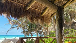 A hammock chair under a thatched roof, overlooking a beach with palm trees and a clear blue sea. - Nueva Vida de Ramiro (Tulum)