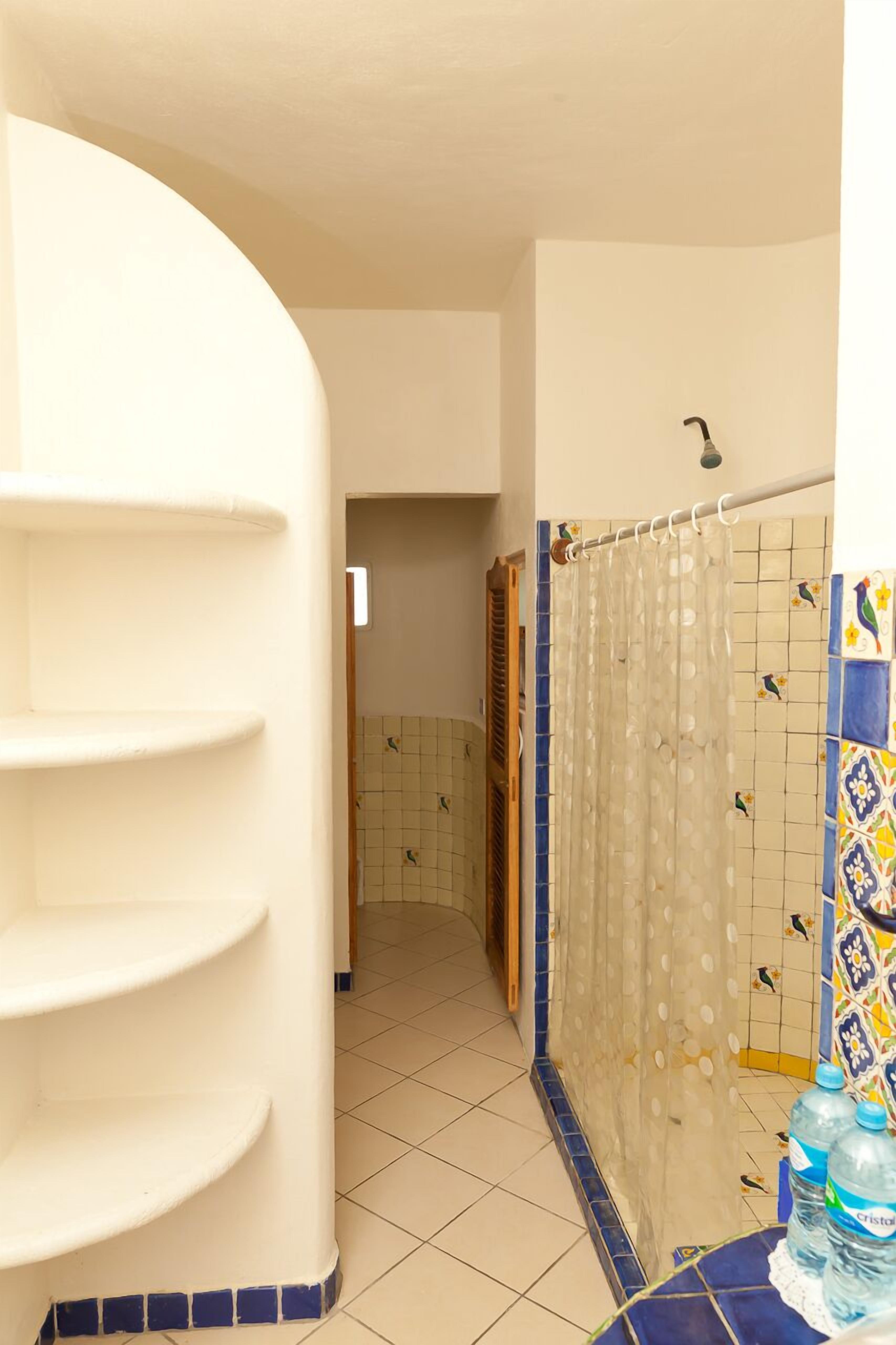A bathroom with a tiled floor, a shower curtain, and a shelf unit.