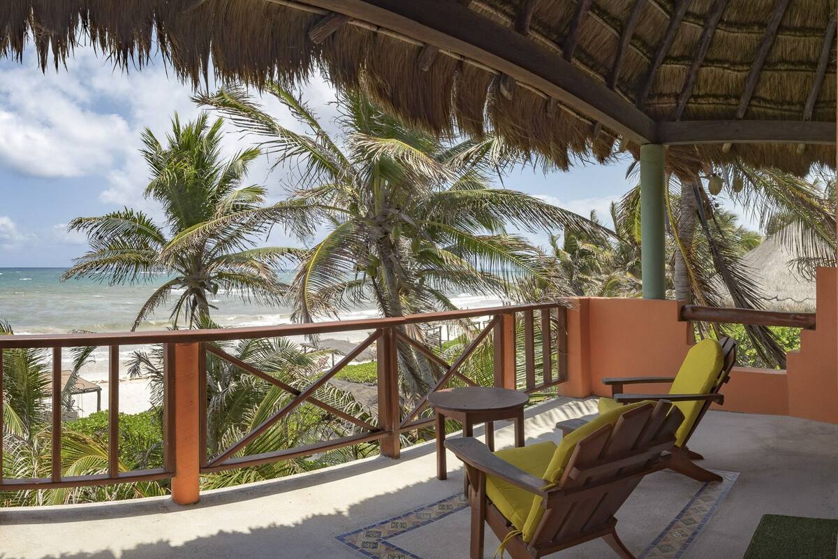 A balcony with a view of the beach and ocean, featuring a wooden chair and a small table.