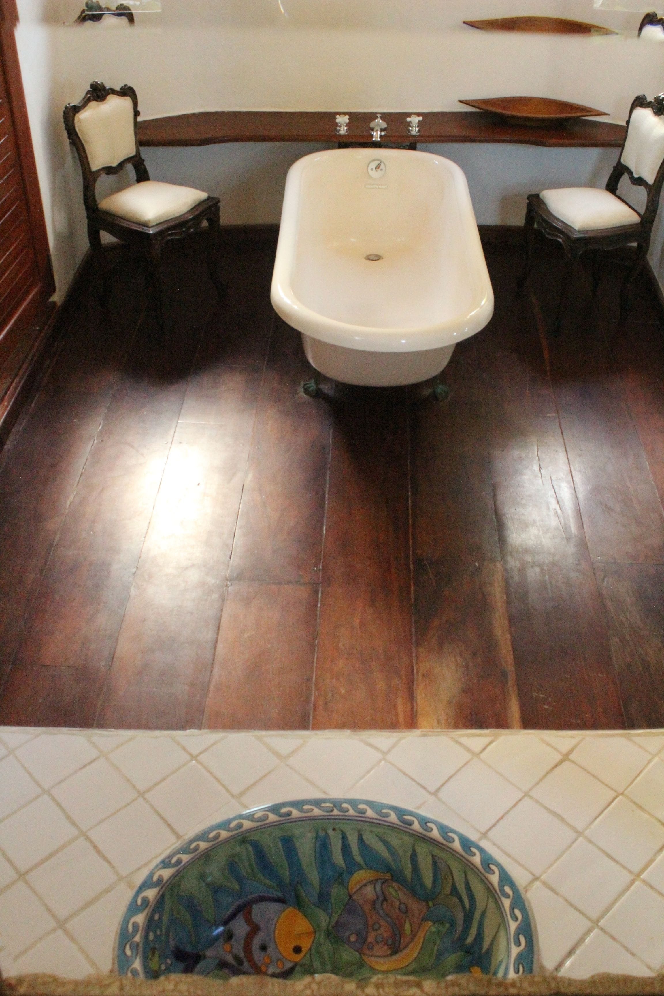 A bathroom with a bathtub, two chairs, and a decorative tile border.