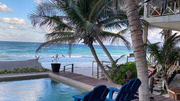 A poolside area with a wooden deck, two blue Adirondack chairs, and a view of the ocean.
