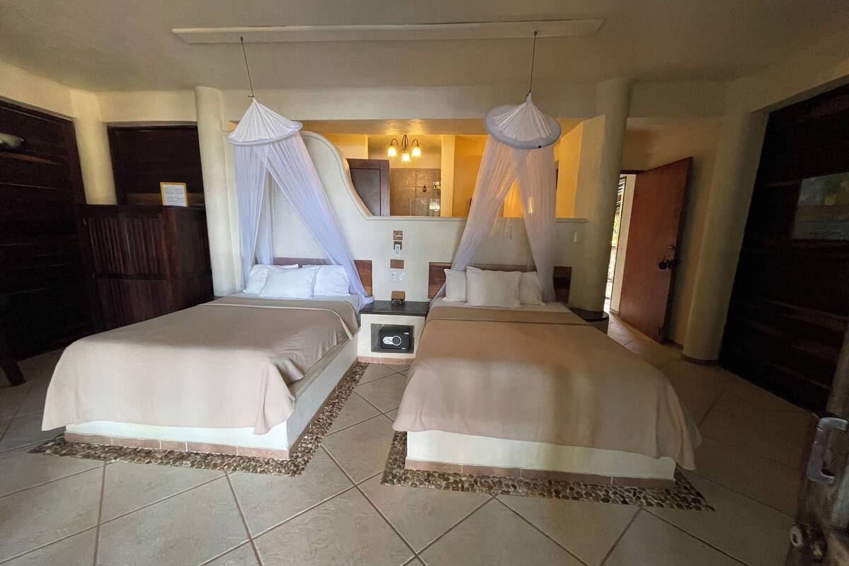 A double room with two beds, each with a canopy, a bedside table, and a small bedside lamp.
