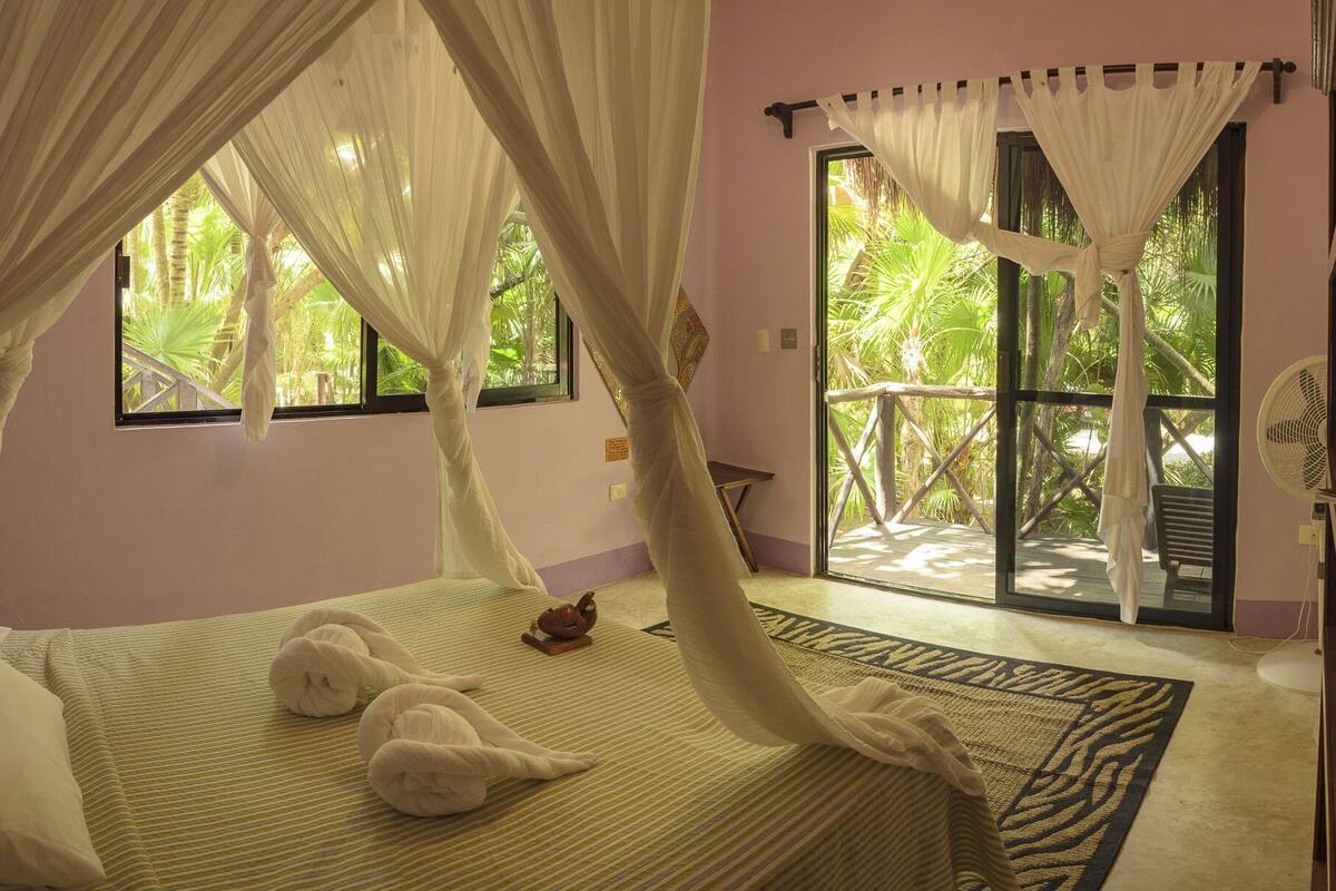 A bedroom with a bed, a window, and a view of greenery outside.