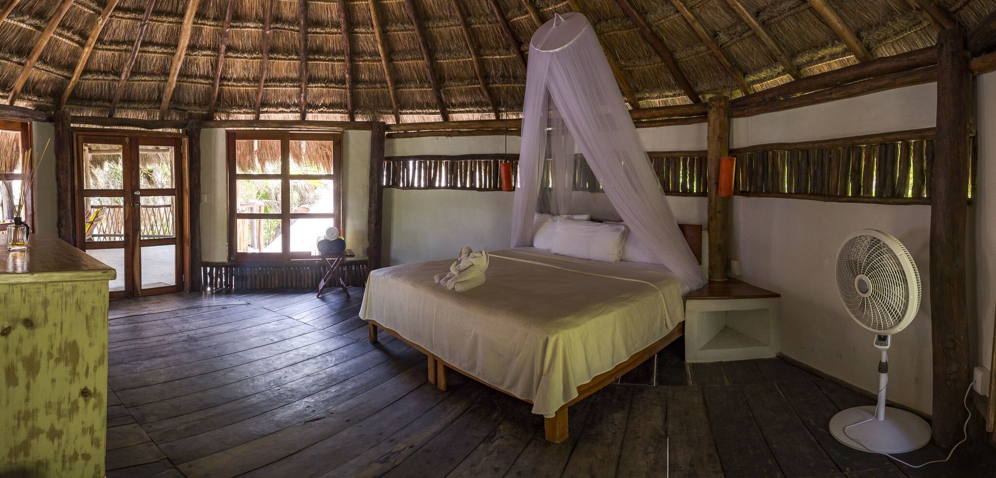 A room with a bed, a bedside table, a fan, and a window.