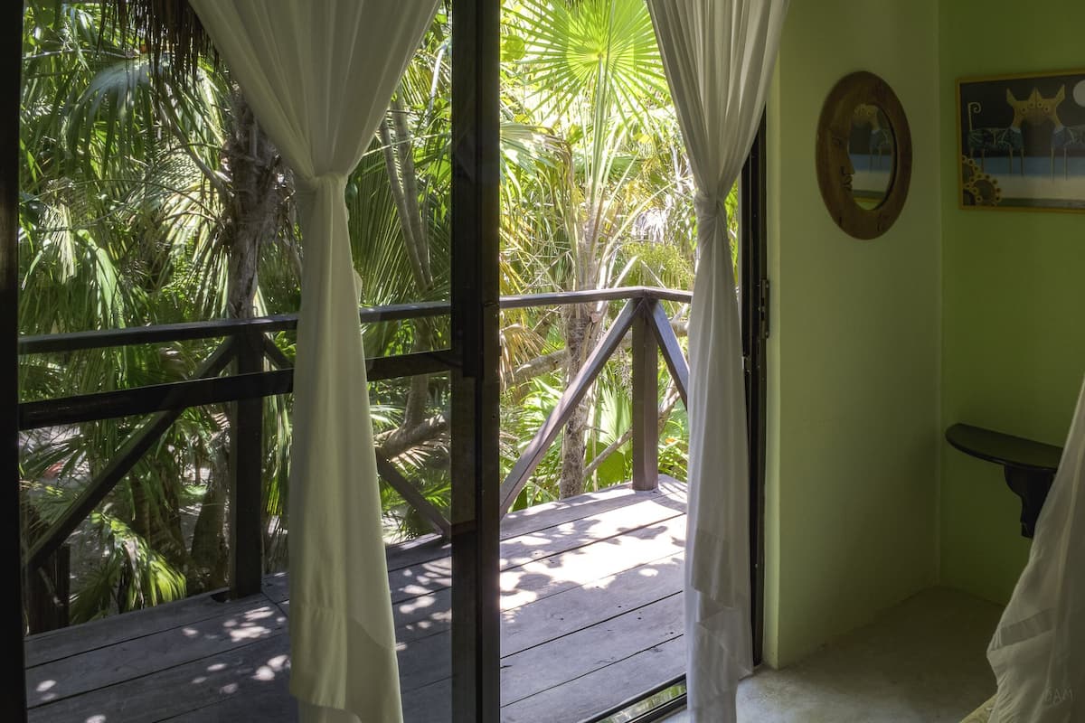 A room with a view of tropical foliage through a window with white curtains.