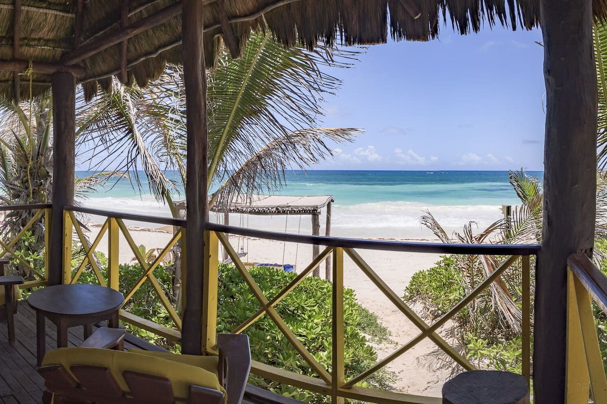 A wooden deck with yellow chairs and a table overlooking a beach.
