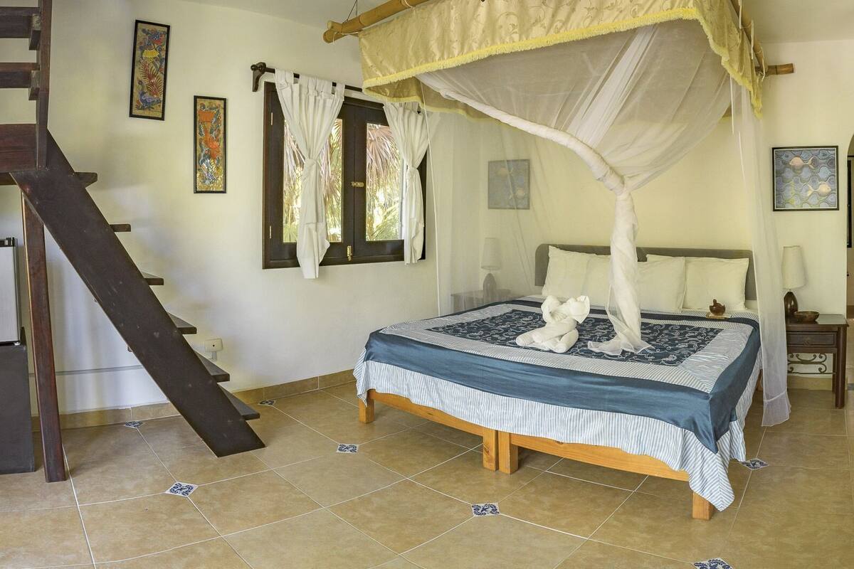 A bedroom with a bed, a staircase, a chair, and a small table.
