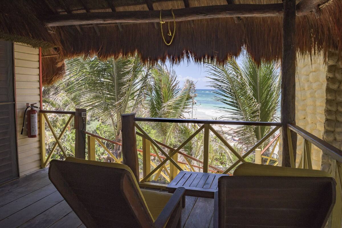 A wooden deck with a thatched roof overlooking a beach.