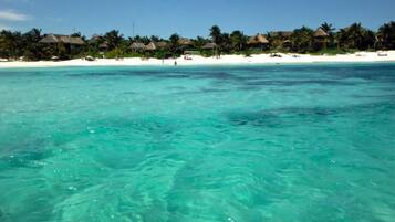 Un resort en la playa con agua turquesa cristalina, arena blanca y cabañas con techo de paja.