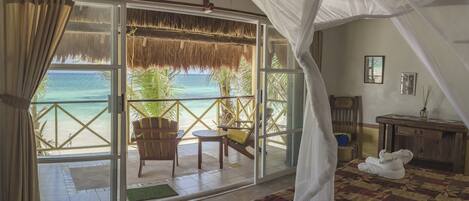 A bedroom with a bed, a chair, a table, and a view of the beach.