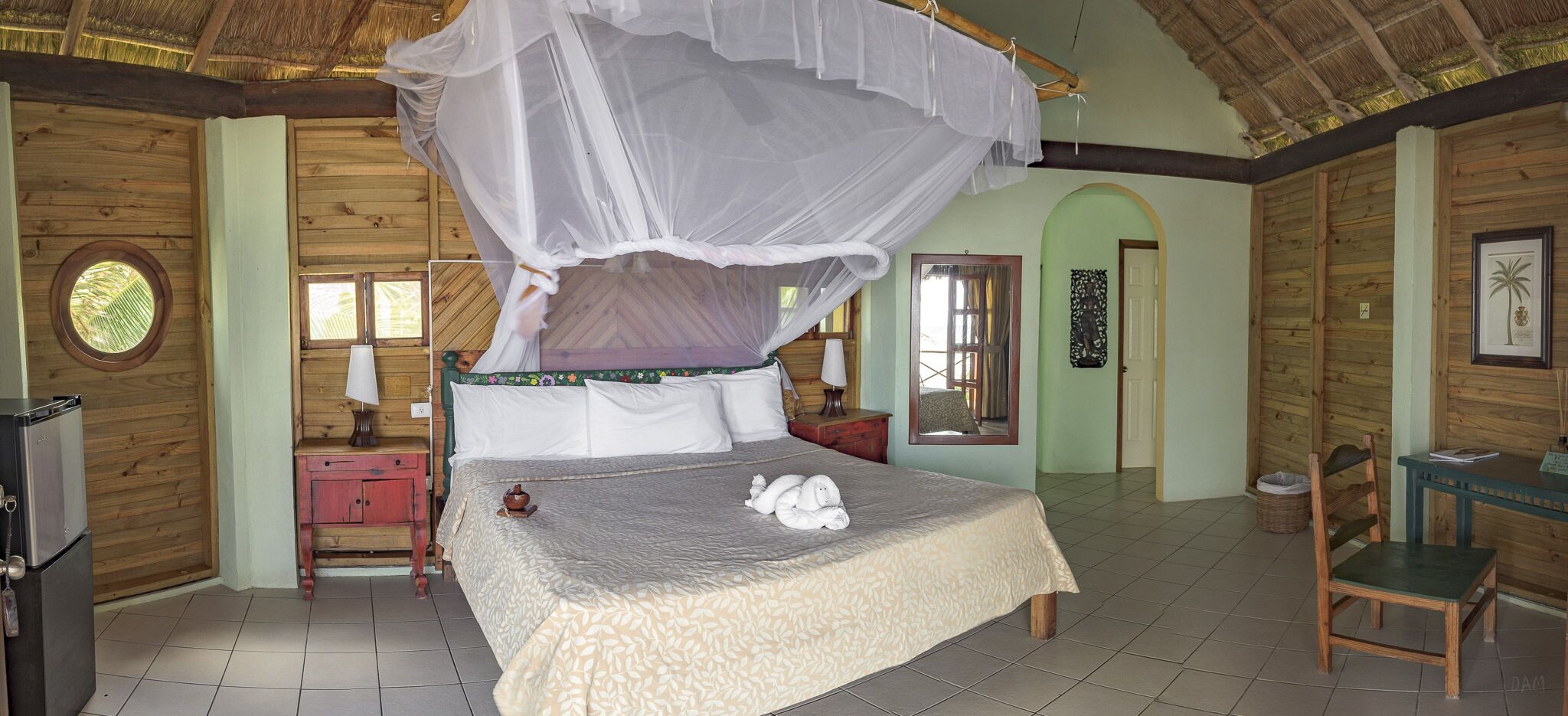 A room with a bed under a canopy, a desk with a chair, and a small table with a chair.