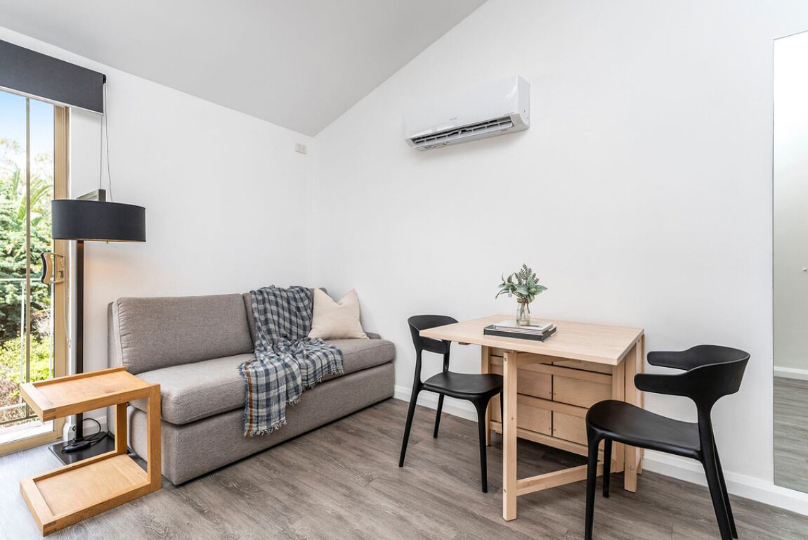 Un salon moderne avec un canapé gris, une table à manger en bois avec deux chaises, une petite table d’appoint et une lampe suspendue.