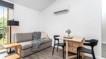 Un salon moderne avec un canapé gris, une table à manger en bois avec deux chaises, une petite table d’appoint et une lampe suspendue.